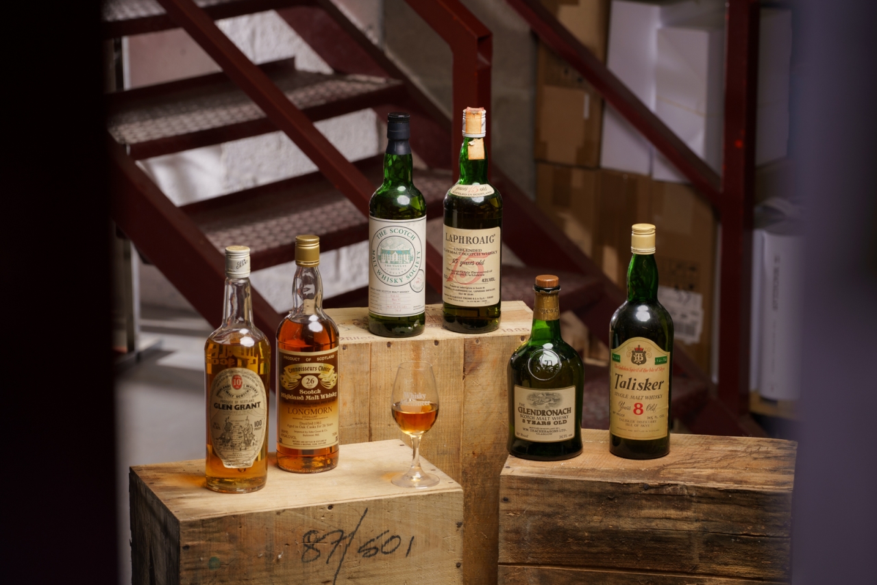 A collection of old and rare whiskies grouped around a whisky auctioneer tasting glass. These are the bottles that will be featured in the tasting event.