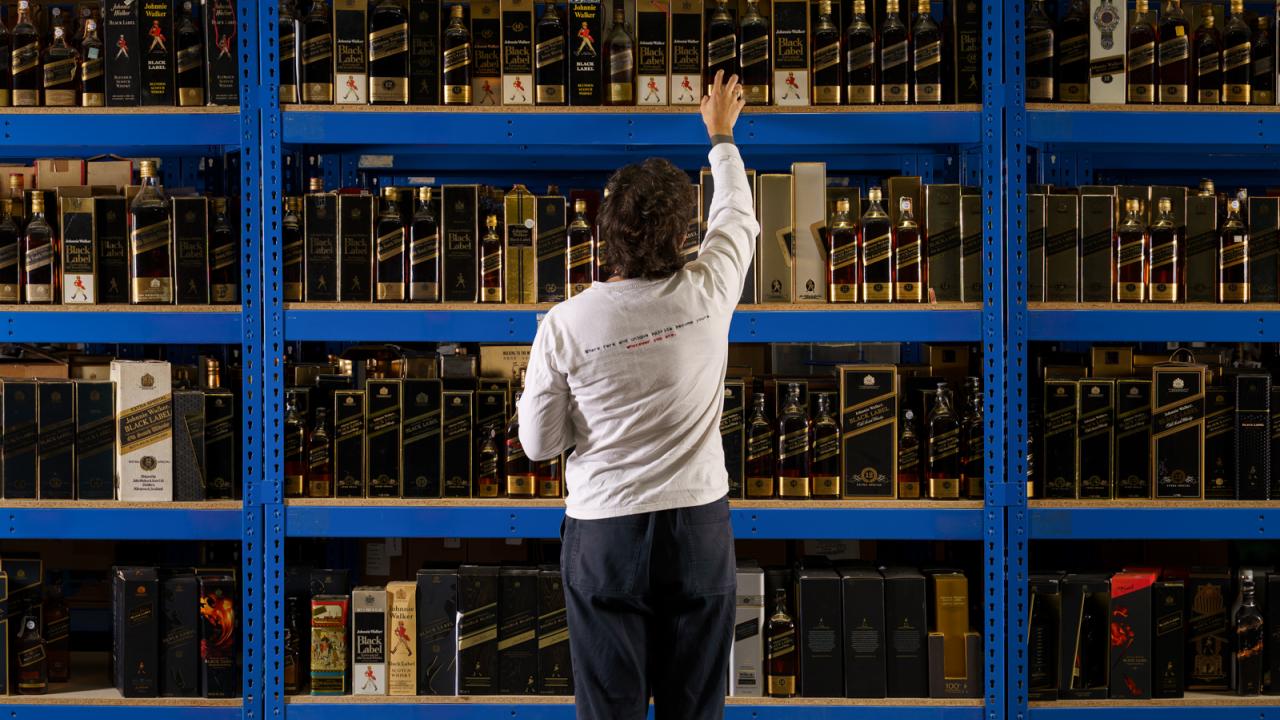 Joe Wilson, Head Curator of Whisky Auctioneer, looking at a wall of bottles on shelves