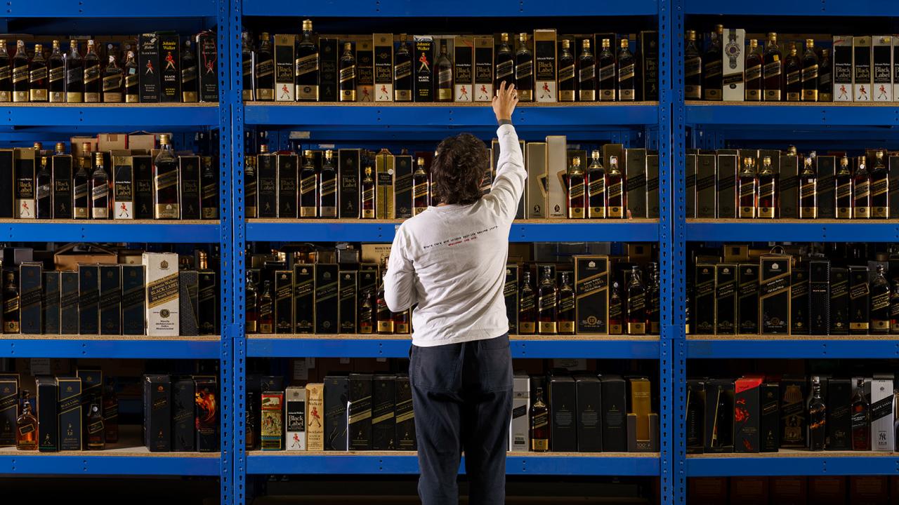 Joe Wilson, Head Curator of Whisky Auctioneer, looking at a wall of bottles on shelves